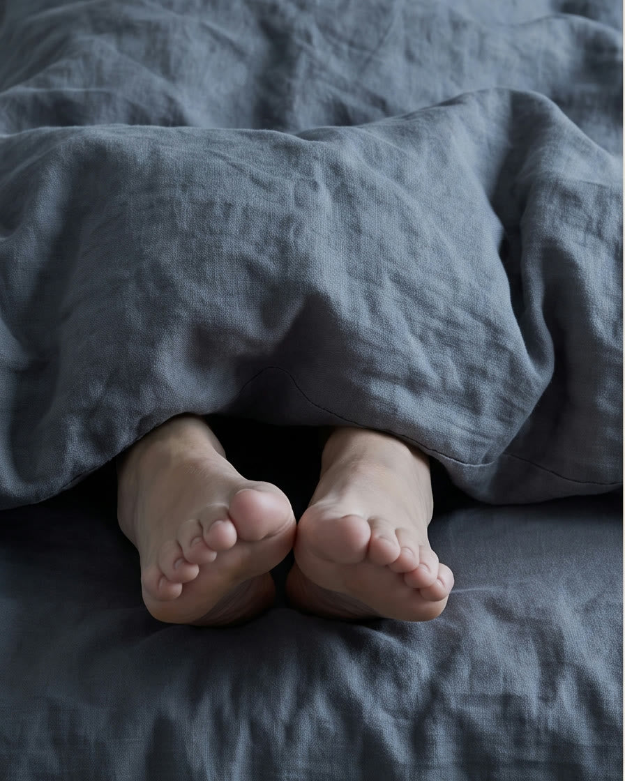 Pieds nus dépassant d'une couette grise dans un lit froid, le soir